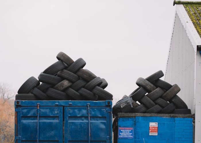 Piles of used tires on blue containers in an industrial recycling yard.